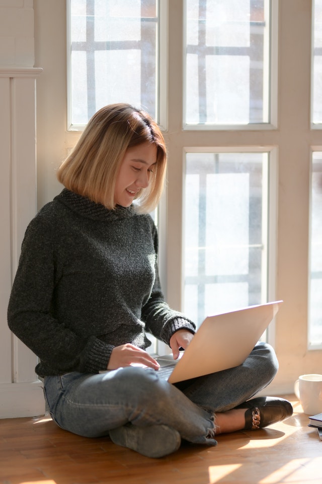 woman-in-gray-sweater-sitting-on-wooden-floor-typing-on-3759115